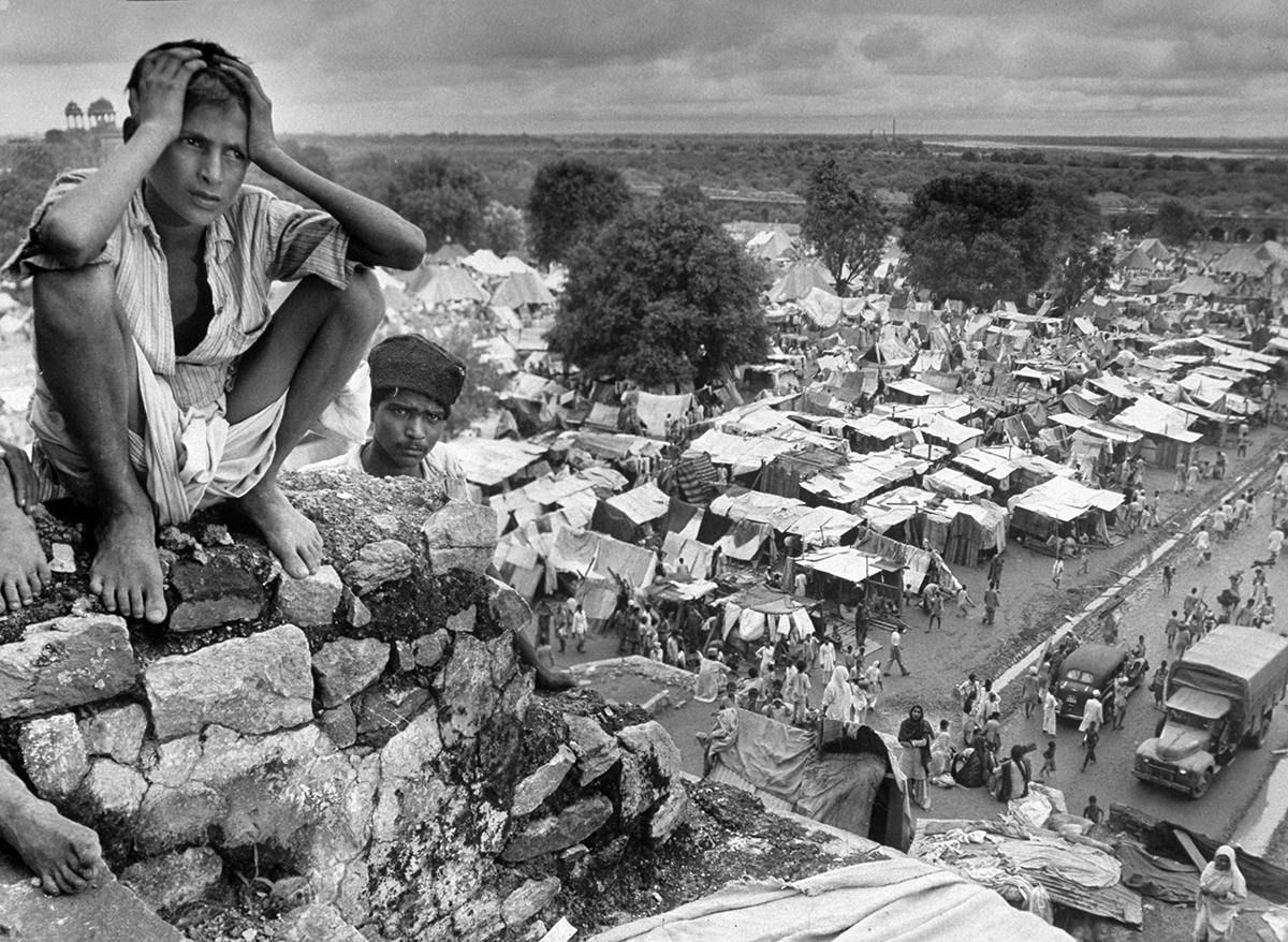 Migration India, October 1947: Boy sitting on rock ledge above refugee camp.